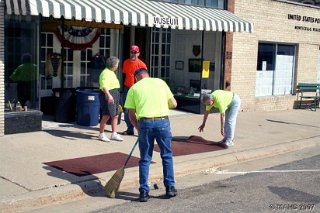 Marlene Schmalbeck talking with passer-by. Donna Ferguson cleaning the floor mats and Bill Dickson tidying the museum entrance before the grand opening.